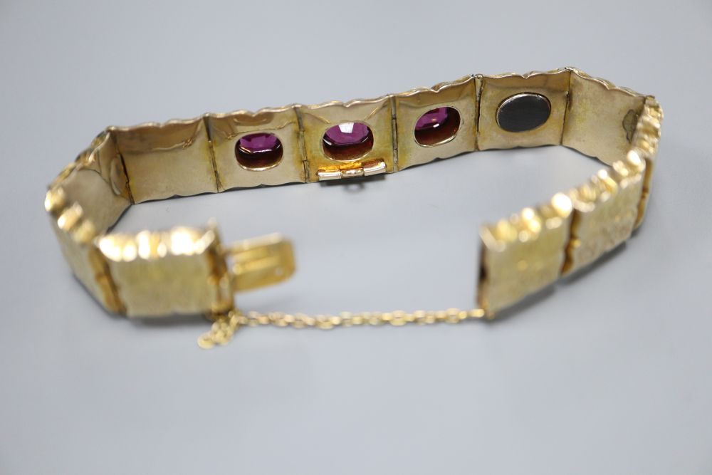 A Victorian engraved yellow metal and three stone garnet set hinged panel bracelet, with safety chain, gross 21.7 grams.